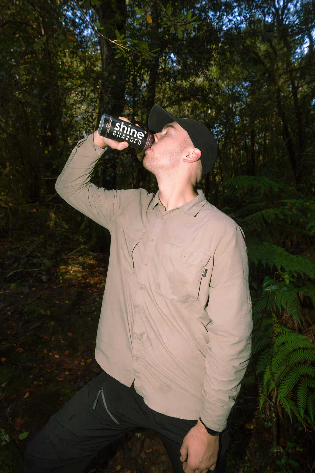 Man drinking nootropic Shine+ Charged energy drink outdoors in a forest setting