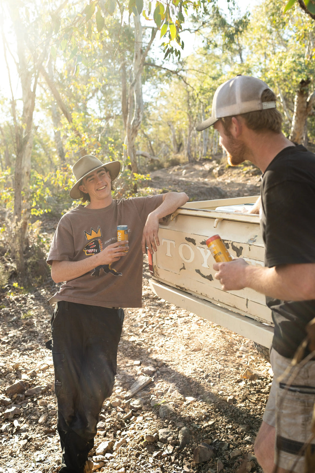 Two men outdoors enjoying nootropic drink cans by a truck in a sunlit forest setting