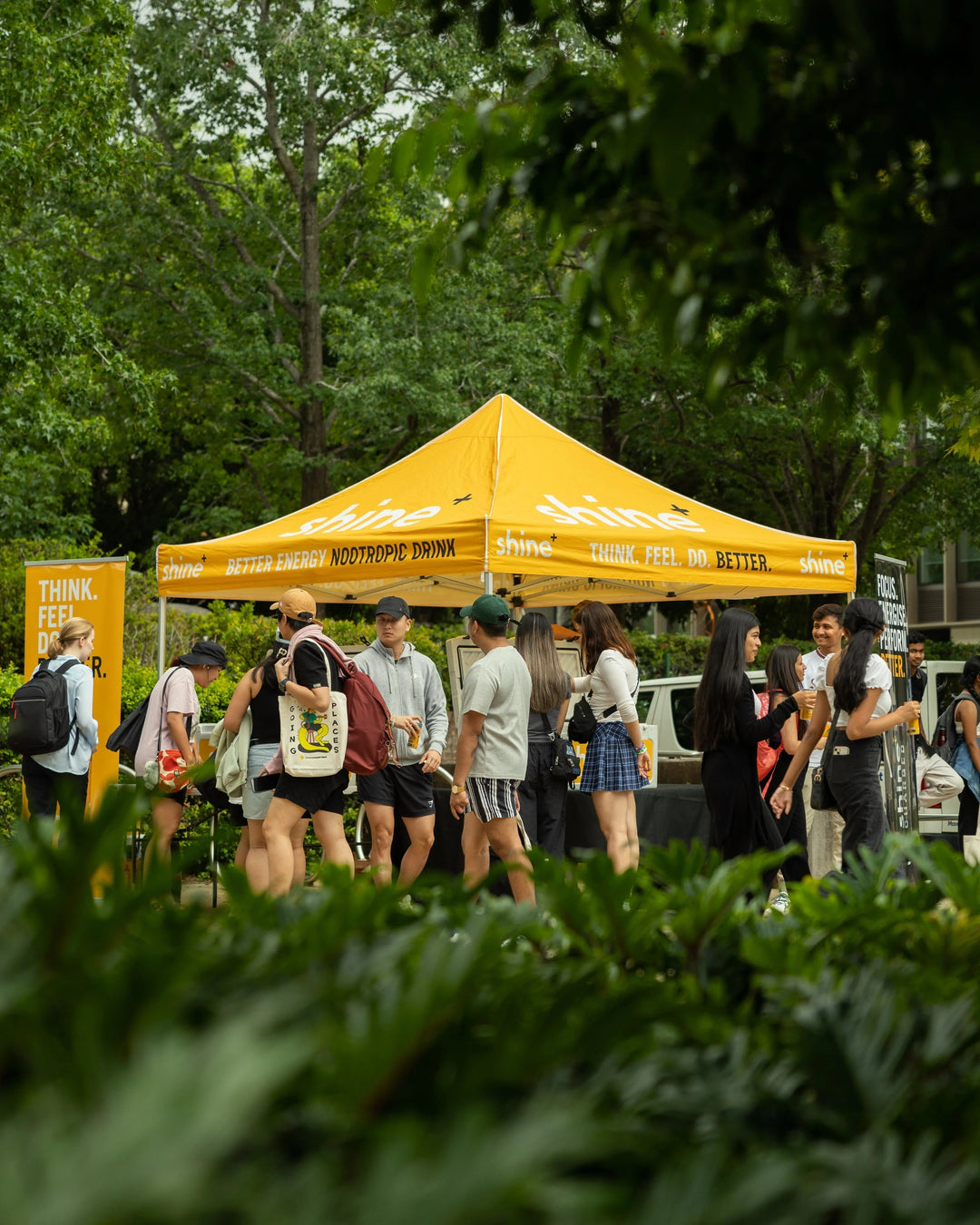 People gathered at a yellow nootropic drink tent outdoors under trees