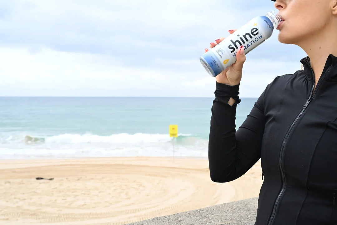 Woman drinking hydration drink at the beach, ocean in background, healthy lifestyle