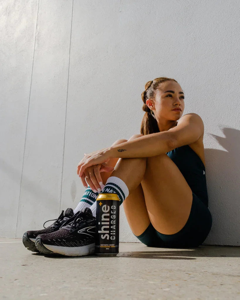 Athletic woman resting outdoors with nootropic energy drink can, running shoes, and sporty outfit