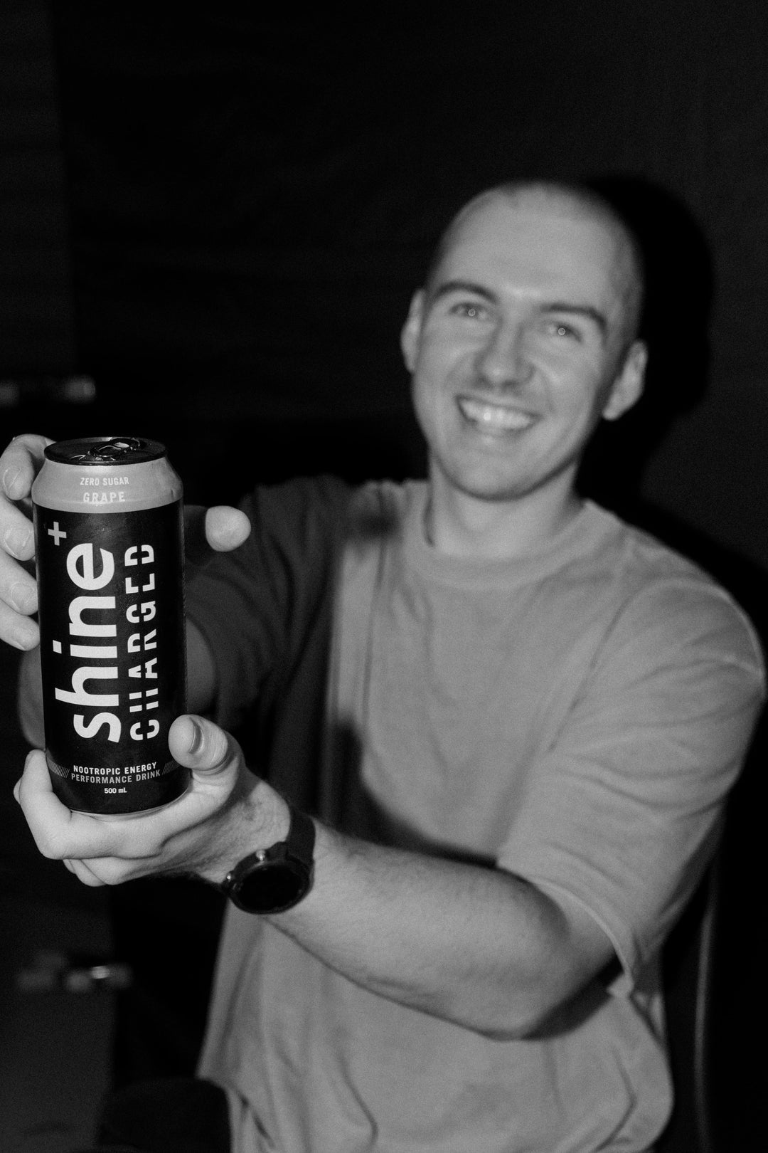 Smiling person holding a can of Shine+ Charged nootropic energy drink, grape flavor.
