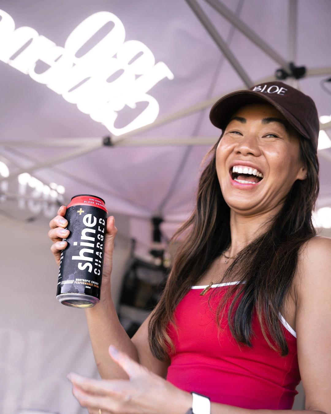Smiling woman holding a can of Shine+ Charged nootropic energy drink at outdoor event