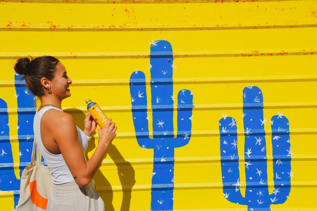 Woman holding nootropic drink bottle in front of yellow wall with blue cactus mural