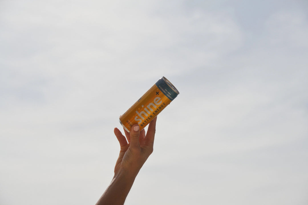 Hand holding a yellow can of natural energy drink against a sky background