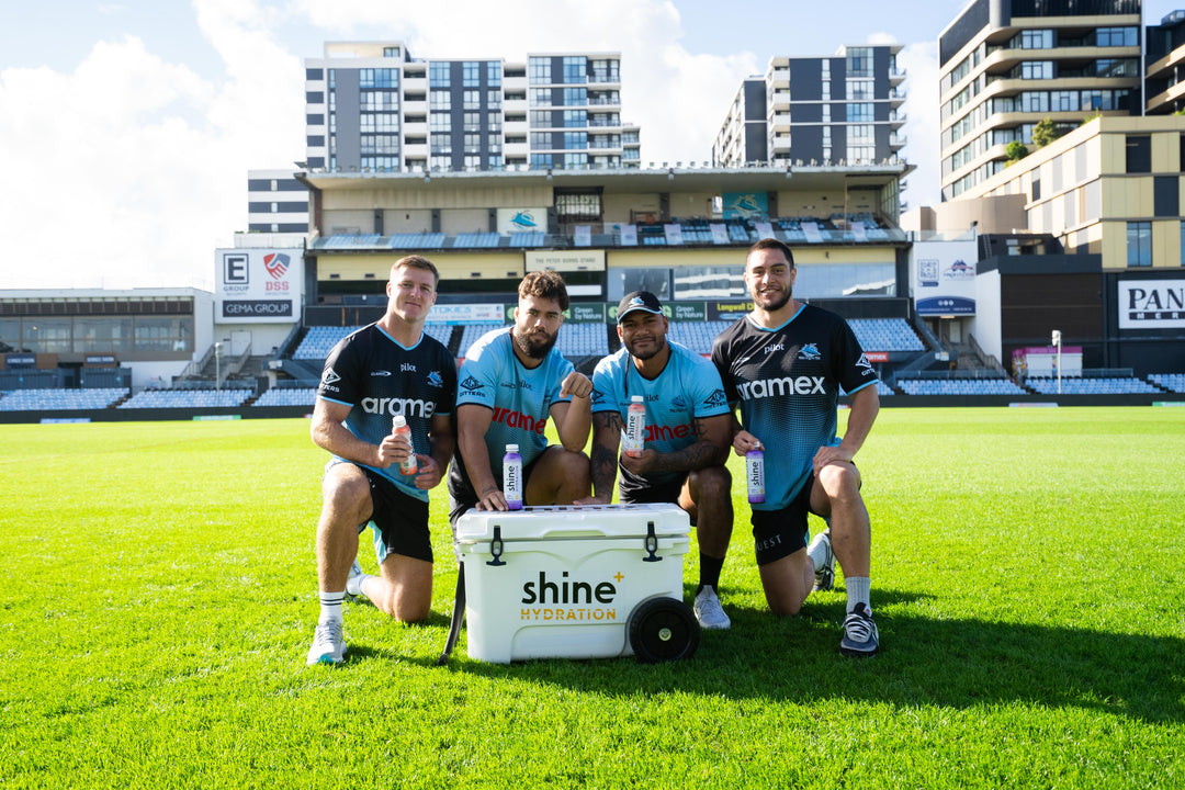 Rugby players on field holding Shine+ nootropic drinks beside a Shine hydration cooler