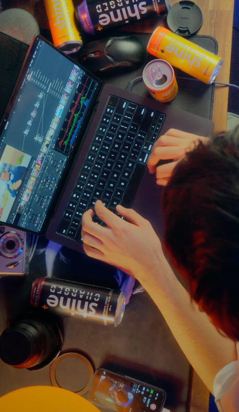 Person editing video on laptop with cans of nootropic drink and camera gear on desk