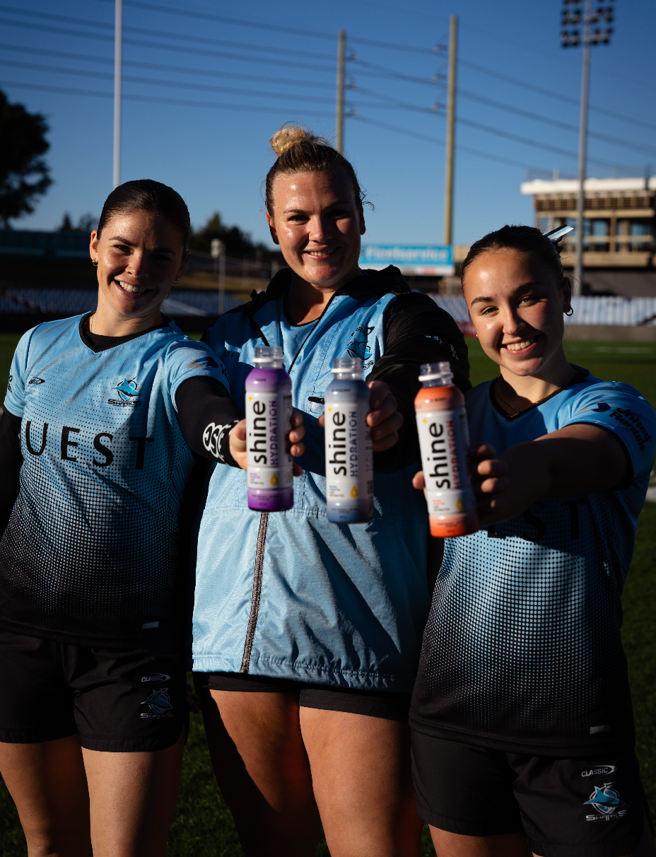 Three athletes in blue jerseys holding bottles of natural nootropic drink on a sports field