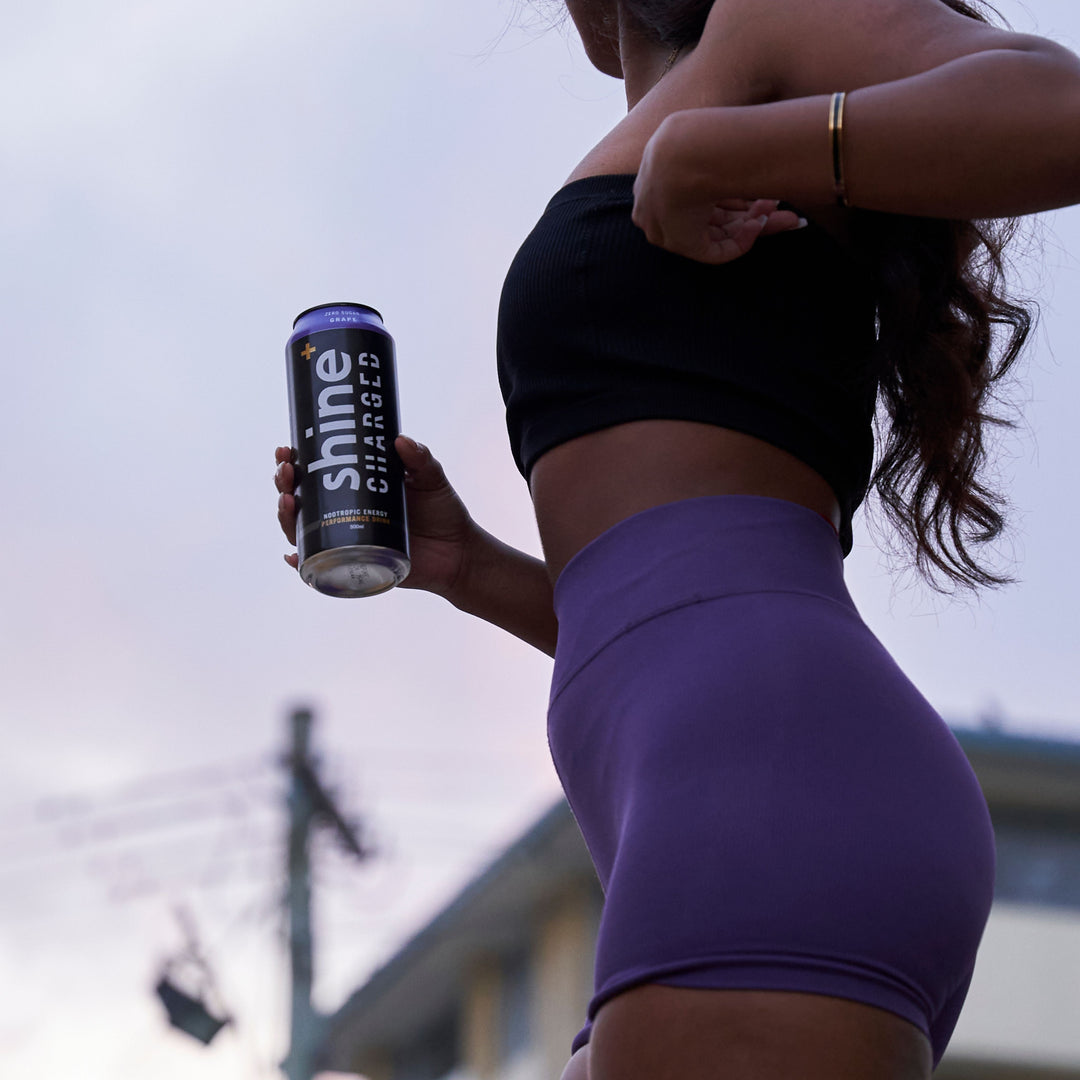 Woman in workout clothes holding Shine Charged nootropic energy drink outdoors