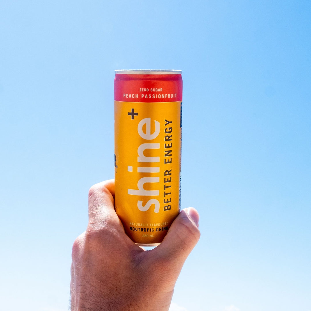 Hand holding a can of nootropic energy drink, peach passionfruit flavor, against blue sky