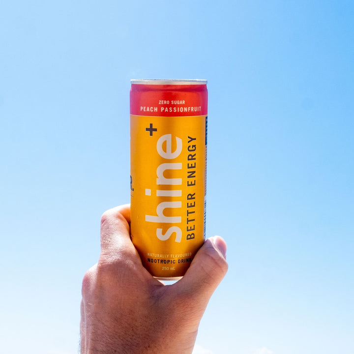 Hand holding a can of nootropic energy drink, peach passionfruit flavor, against blue sky