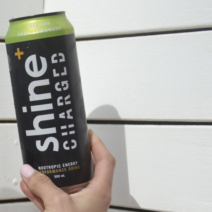 Hand holding a can of zero sugar yuzu lemonade nootropic energy drink against white wall