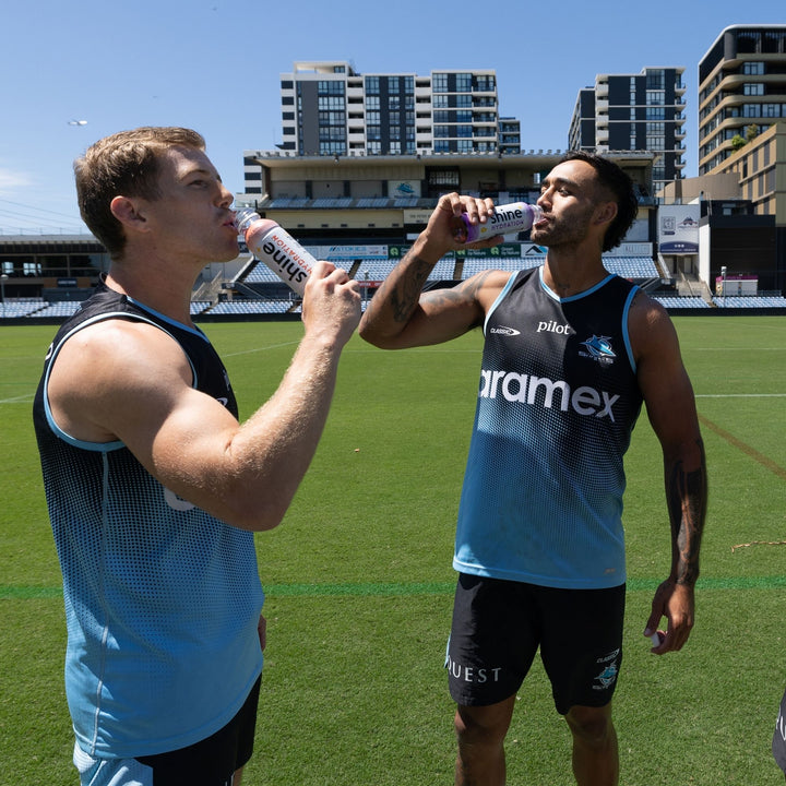 Two athletes in sportswear drinking nootropic hydration drinks on a football field