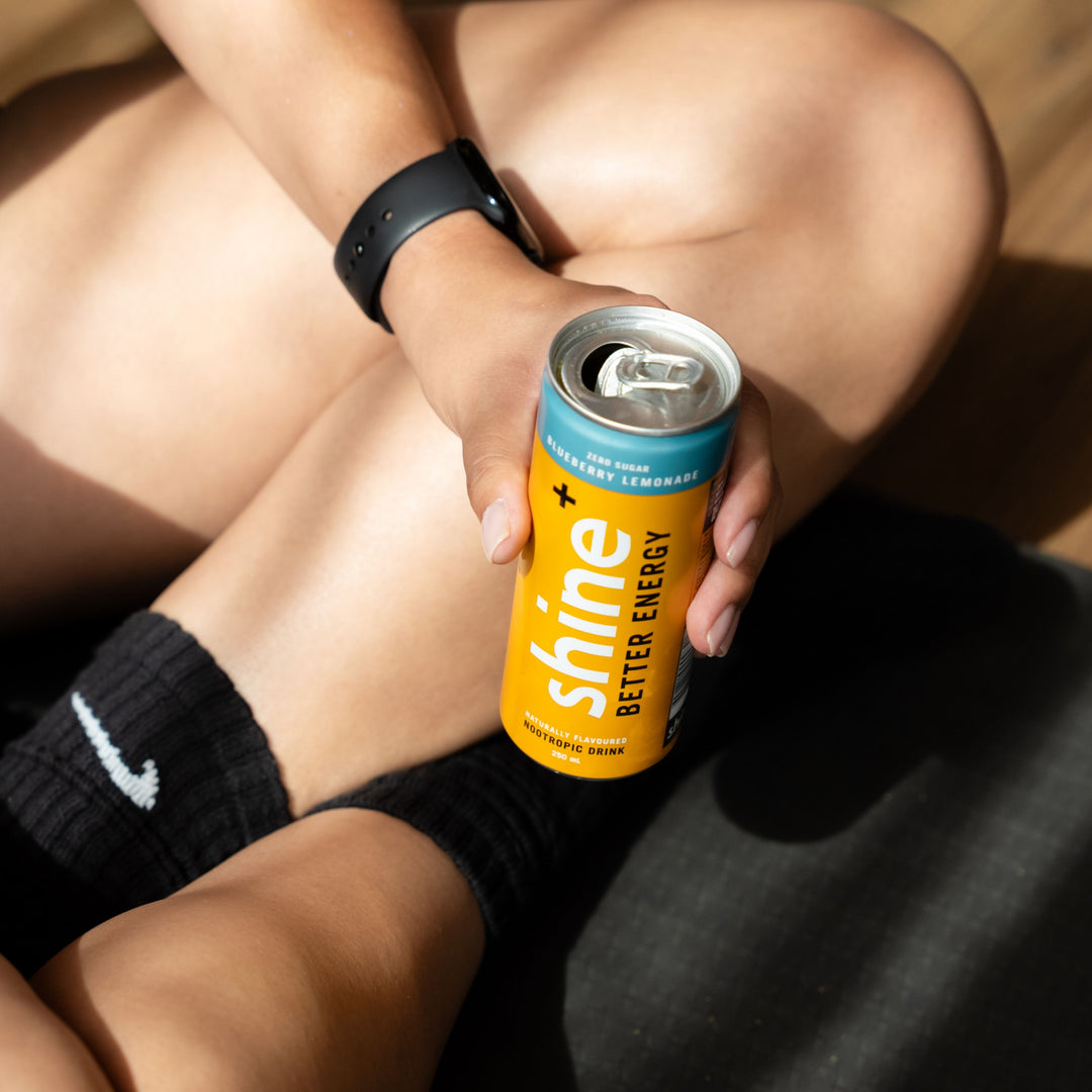 Hand holding a Shine blueberry lemonade nootropic drink can, seated on yoga mat